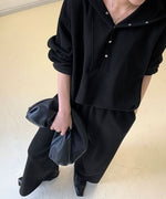 黒のボタン付きフーディとワイドパンツのセットアップを着用した女性の、ボタン開きの胸元クローズアップ。
