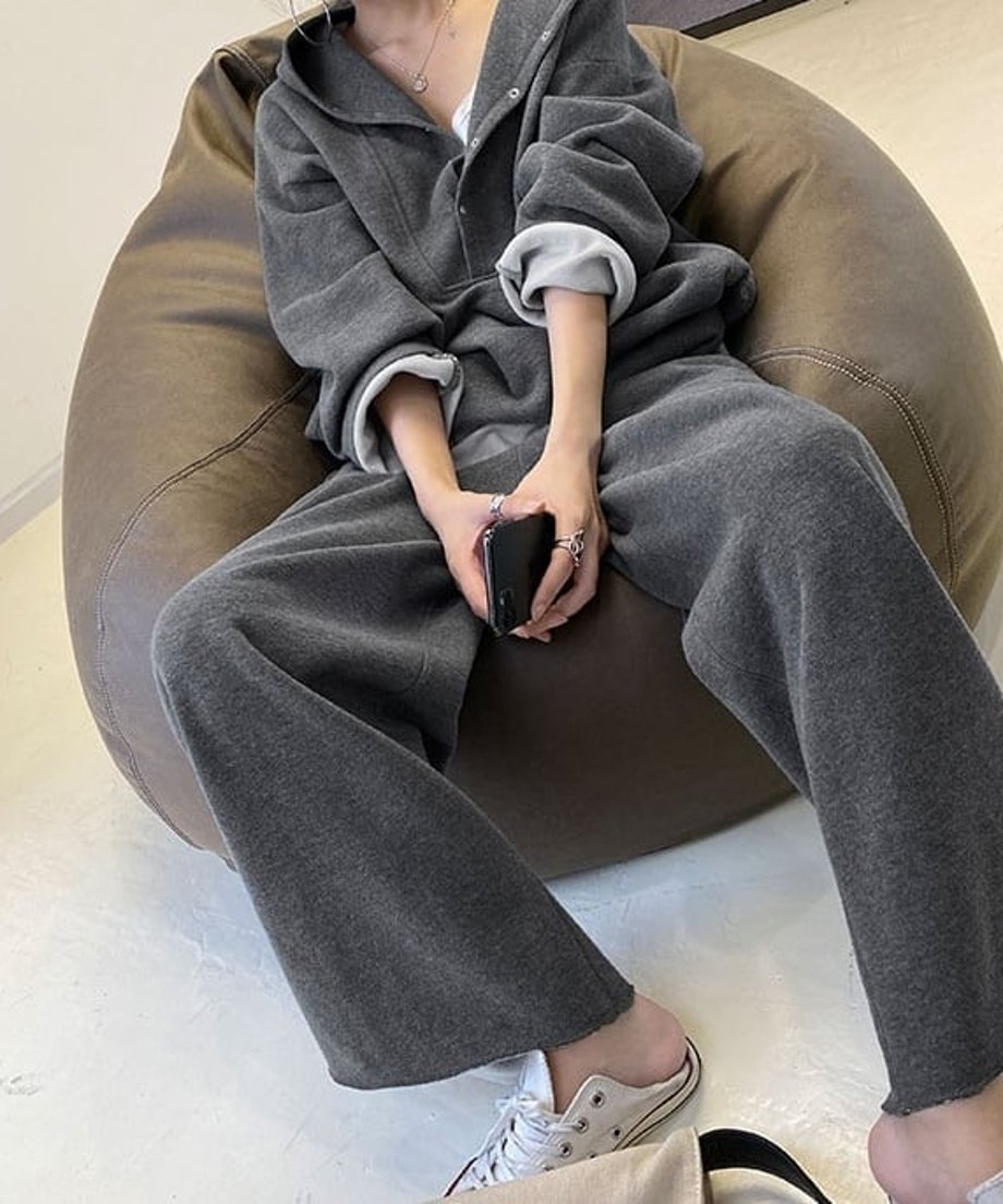 グレーのボタン付きフーディとワイドパンツのセットアップを着用した女性が、ビーズクッションに座っている全身像。白いスニーカーを履いている。
