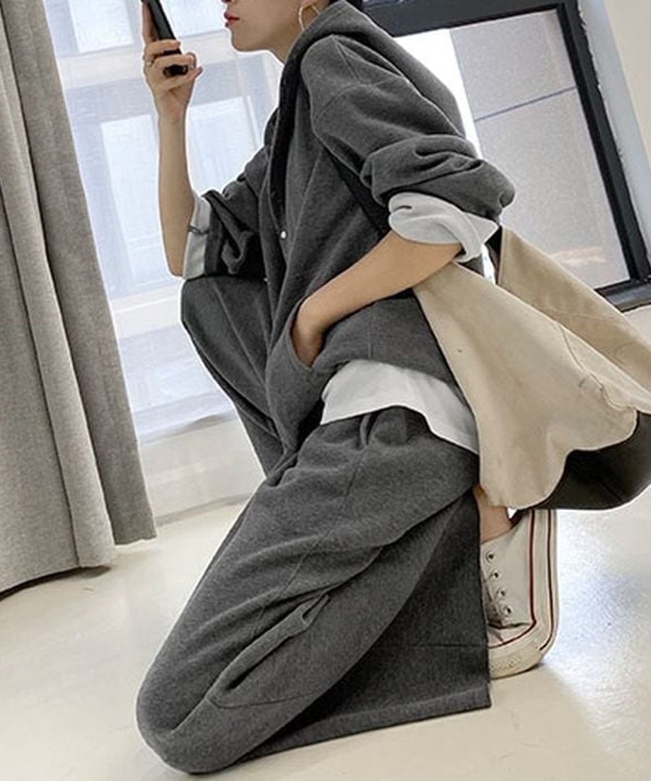 グレーのセットアップを着用し、床にしゃがむなどリラックスしたポーズをとる女性。ワイドパンツのゆったりとしたシルエットがわかる。
