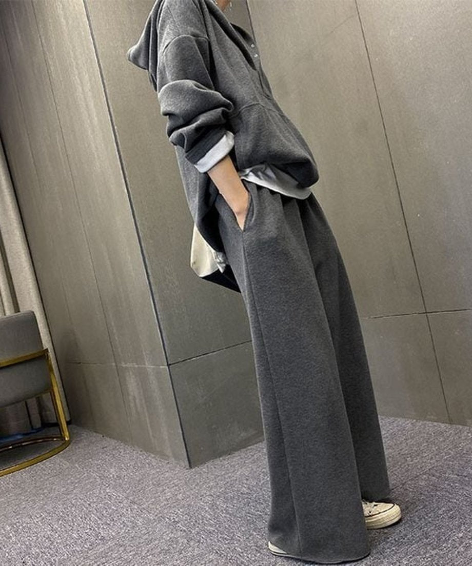 グレーのワイドパンツの裾が床に届くほどのフルレングスで、体型をカバーするルーズなシルエットを写した画像。