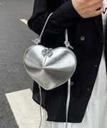 シルバーのメタリックなハート型ミニバッグを手に持っているクローズアップ画像。バッグには短い持ち手と長いショルダーストラップが付いている。