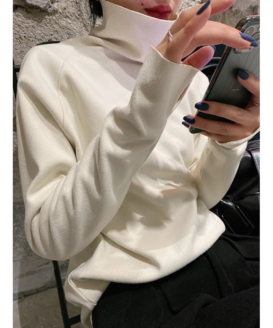 オフホワイト色のタートルネックトップスを着用した女性が座っているアップ画像。