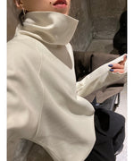 オフホワイトのタートルネックトップスを着用した女性の腕のクローズアップ画像。袖口のスリットがみえる。