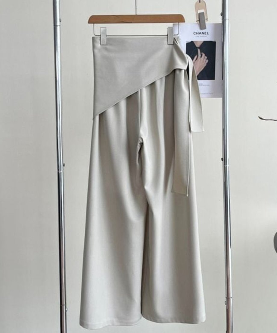 オフホワイトのワイドレッグパンツがハンガーにかかっている後ろ姿。スカーフを巻いたエストデザインが強調されている。