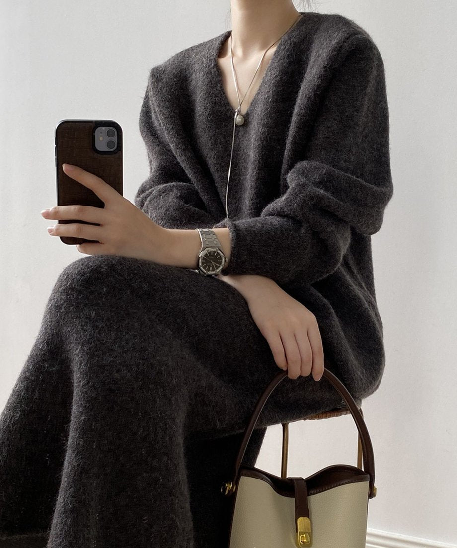 チャコールのVネックニットセットアップを着用し座っている女性のクローズアップ。スマートフォンと白×茶色のバケツ型バッグを持っている。