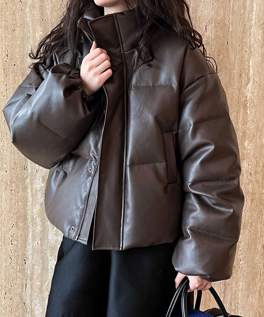 コーヒーのPUレザーショート丈ダウンジャケットを着用した女性の上半身。ボトムスは黒色のワイドパンツを合わせ、黒いバッグを持っている。