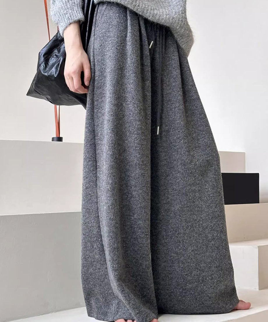 グレーのワイドニットパンツとグレーのニットトップスを着用し、黒いバッグを持つ女性の立ち姿。
