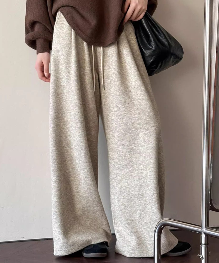 オフホワイトのワイドニットパンツとブラウンのニットトップスを着用し、黒のバッグを持つ女性の立ち姿。