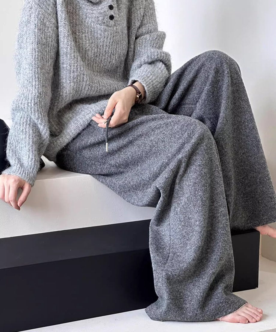 グレーのワイドニットパンツとリブ編みのグレーニットを着用し、ベンチに座っている女性の全身。