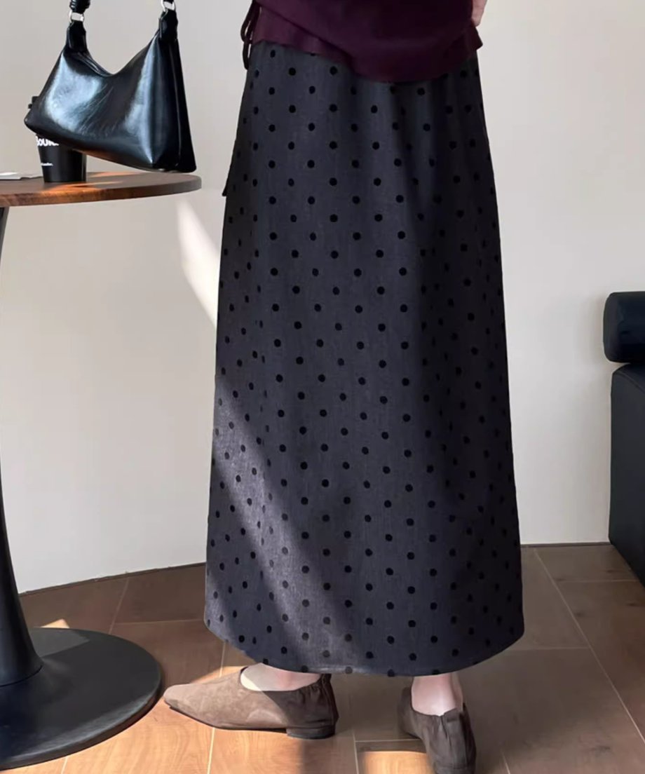 黒いドット柄のグレーロングスカートと、ワインレッドのトップス、スエード調のフラットシューズを着用した女性の膝下の後ろ向きショット。