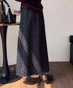 黒いドット柄のグレーロングスカートと、ワインレッドのトップス、スエード調のフラットシューズを着用した女性の後ろ姿の膝下ショット。