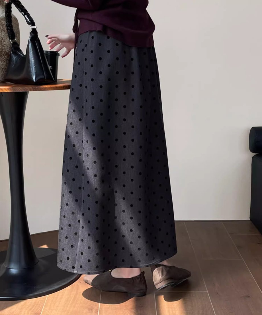 黒いドット柄のグレーロングスカートと、ワインレッドのトップス、スエード調のフラットシューズを着用した女性の後ろ姿の膝下ショット。