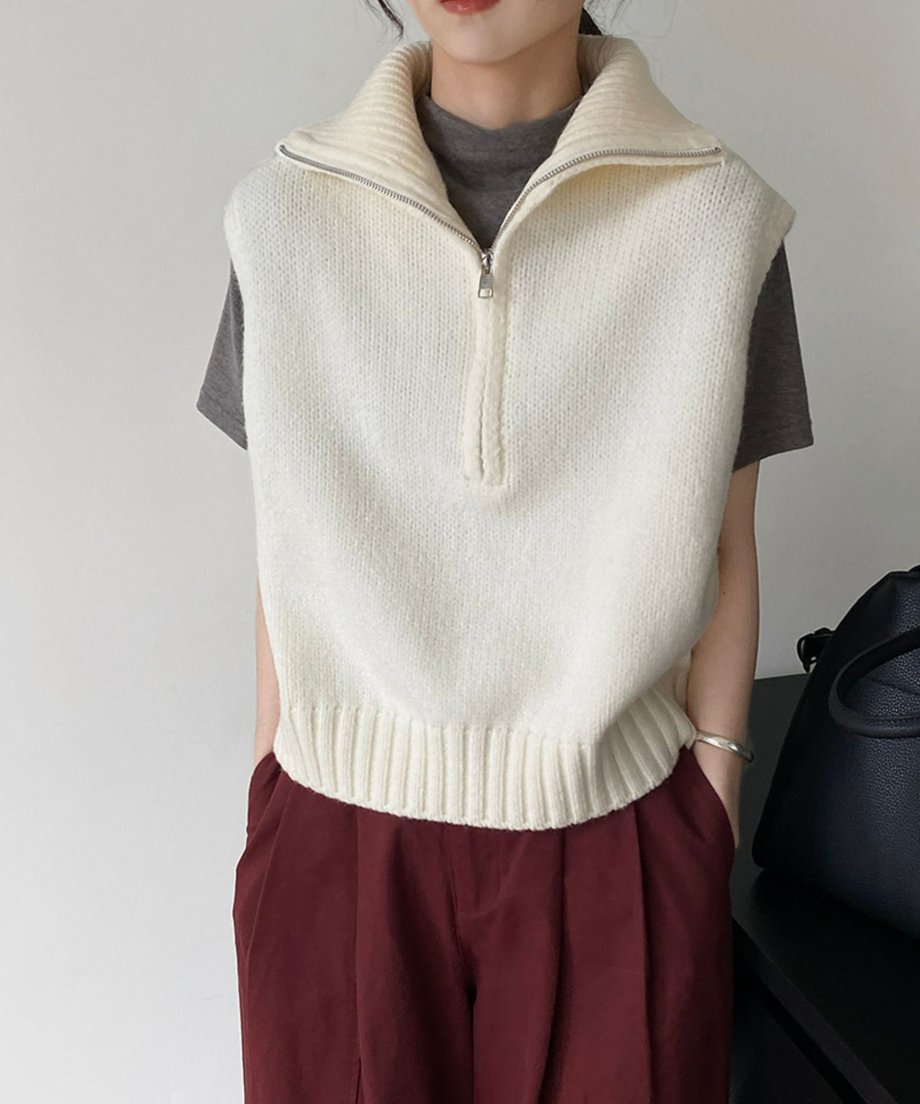 ホワイトのハーフジップニットベストを着用し、ボルドーのパンツを合わせた女性。シルバーのバングルを着用した上半身のクローズアップ。