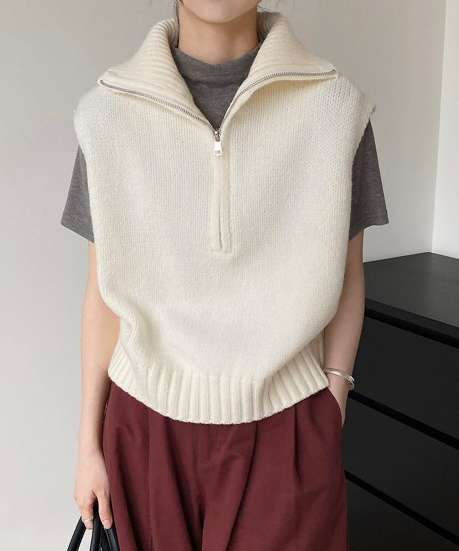ホワイトのハーフジップニットベストをチャコールグレーのTシャツの上に重ね、赤茶色のワイドパンツと合わせた全身コーディネート。