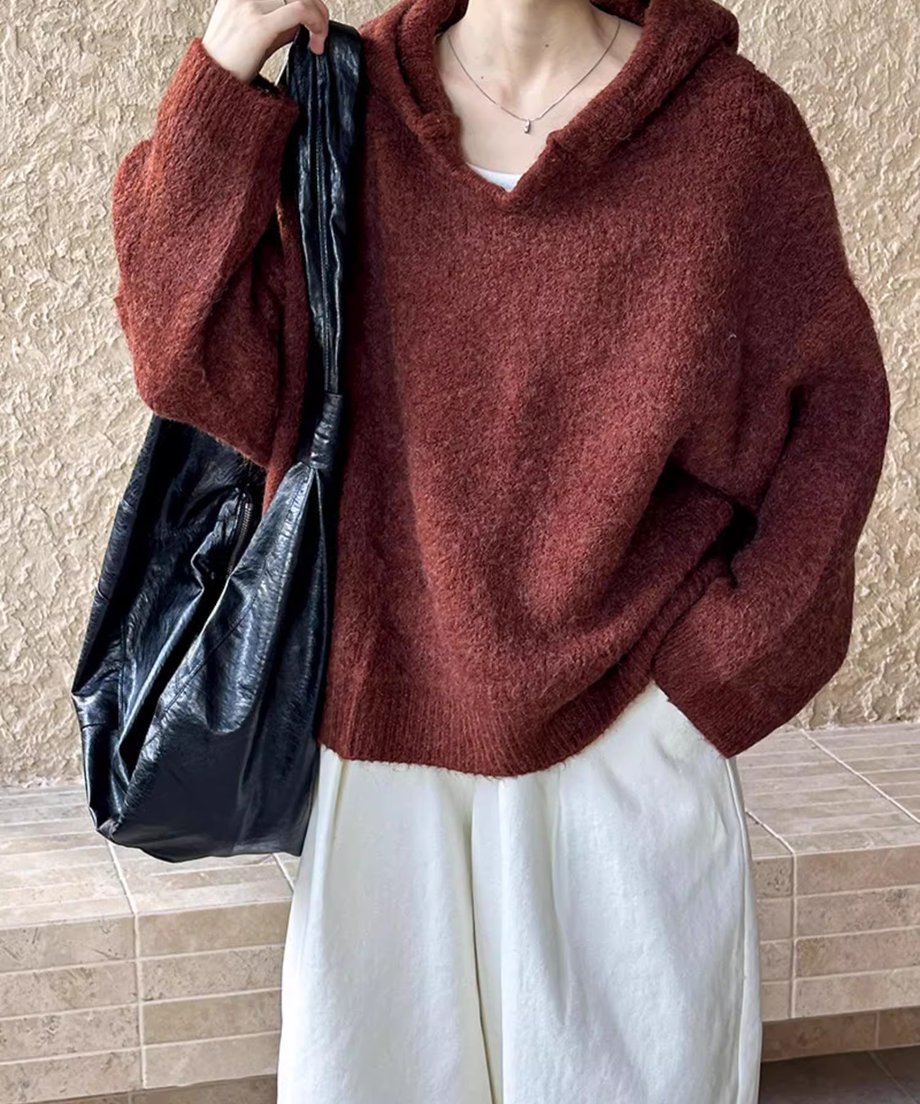 ブラウンのVネックフーディニットに、白のワイドパンツを合わせ、黒のバッグを持つ女性のショット。