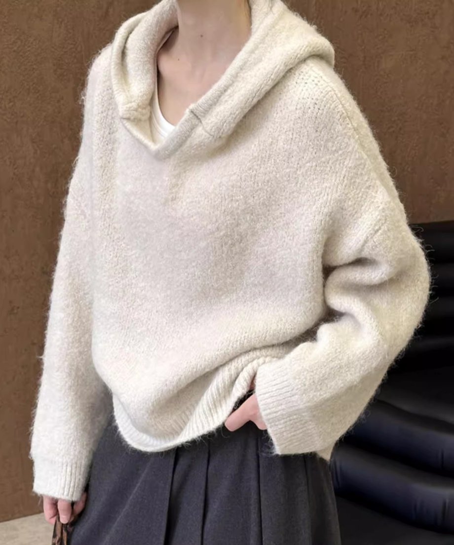 ホワイトのふんわりとしたフーディニットを着用し、濃いグレーのスカートを合わせた女性。
