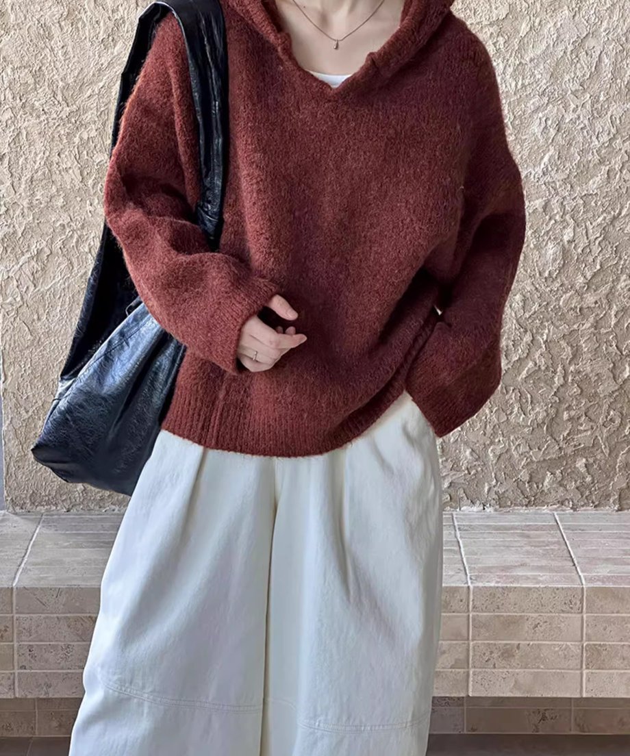 ブラウンのVネックフーディニットに、白のワイドパンツを合わせ、黒のバッグを持つ女性の全身ショット。