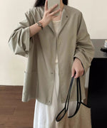 ノーカラーショートコートに白のインナーとボトムスを合わせた女性がスマホを持った室内ショット。