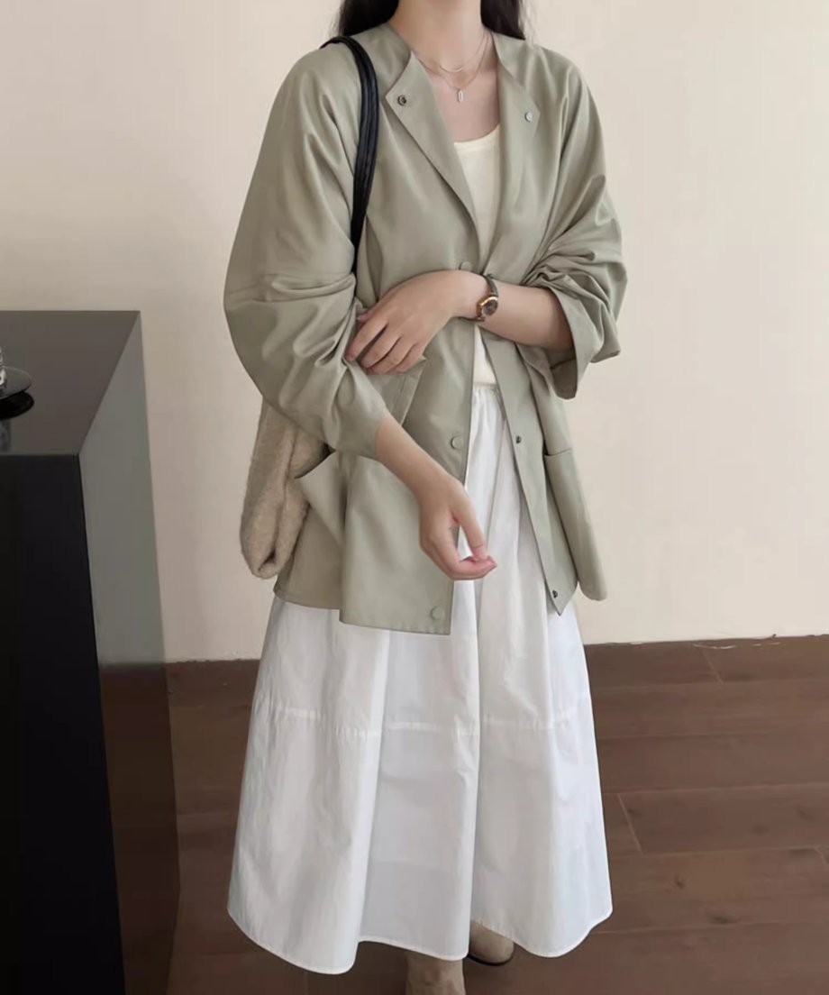 カーキグリーンのノーカラーショートコートに白のインナーと白のスカートを合わせた女性の全身ショット。