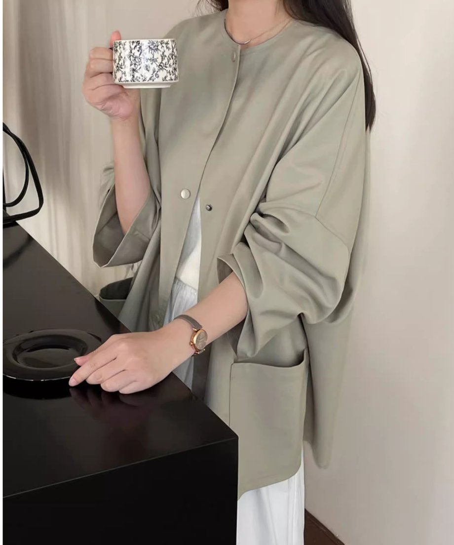 ノーカラーショートコートに白のインナーと白のスカートを合わせた女性の上半身ショット。