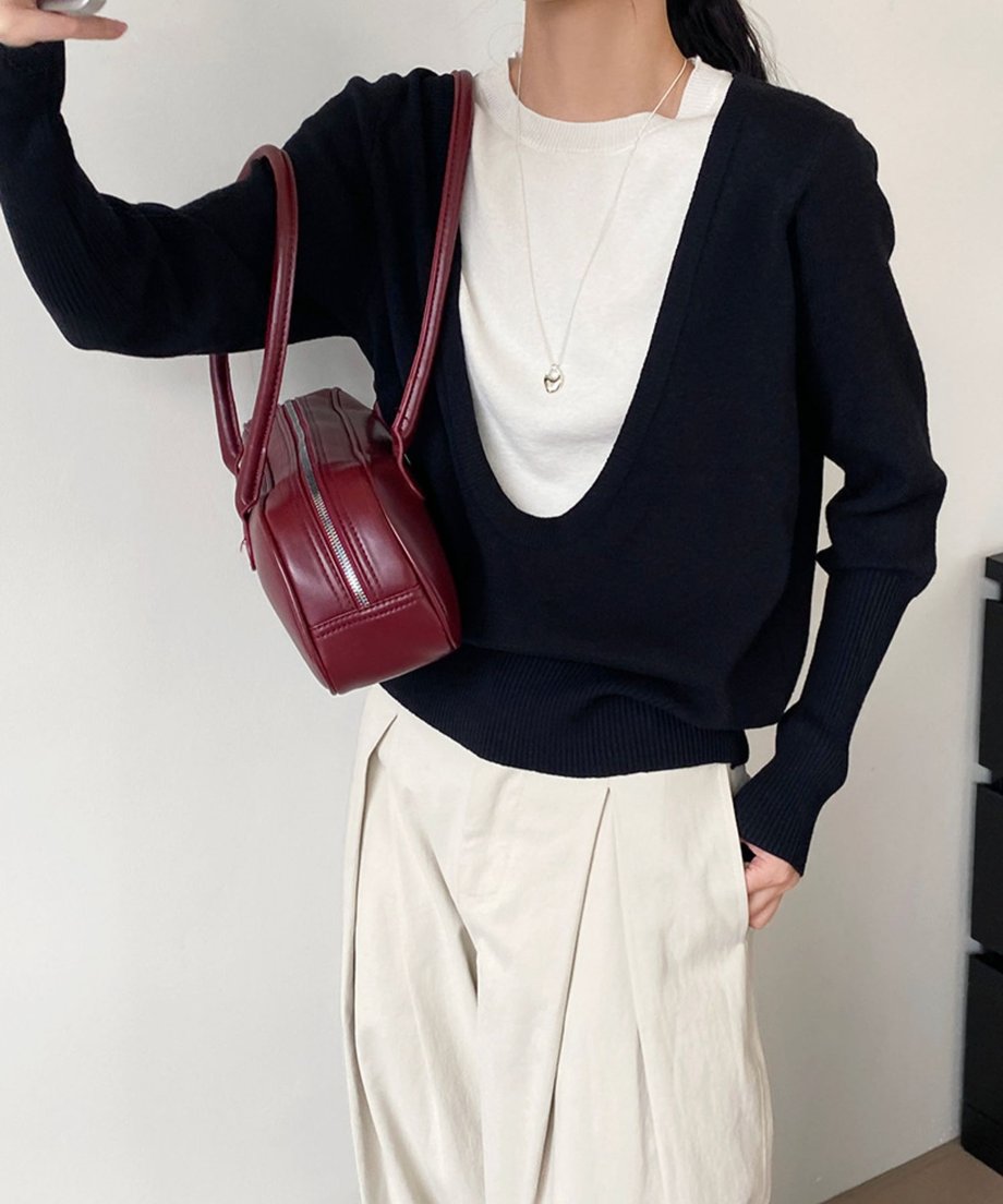 黒のワイドネックフェイクレイヤードニットと白のインナーに、ライトベージュのプリーツワイドパンツを合わせた女性。ボルドー色のバッグを肩にかけている全身ショット。