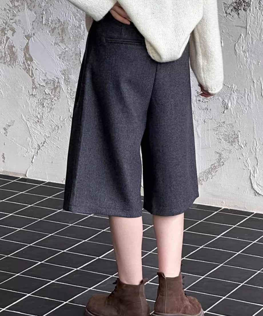 グレーのワイドハーフパンツを着用し、白のニットとブラウンのレースアップブーツを合わせた後ろ向きのショット。