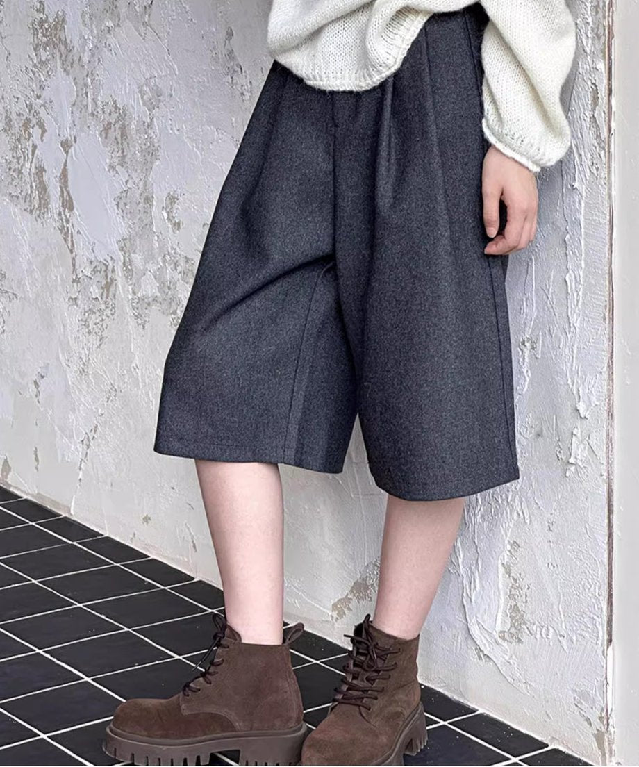 壁にもたれかかるグレーのワイドハーフパンツの着用画像。ゆったりとしたシルエットが特徴。