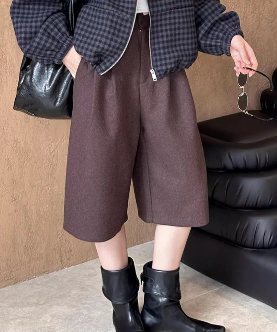 ブラウンのワイドハーフパンツとチェック柄ブルゾン、黒のブーツの着用画像。手にサングラスを持っている。