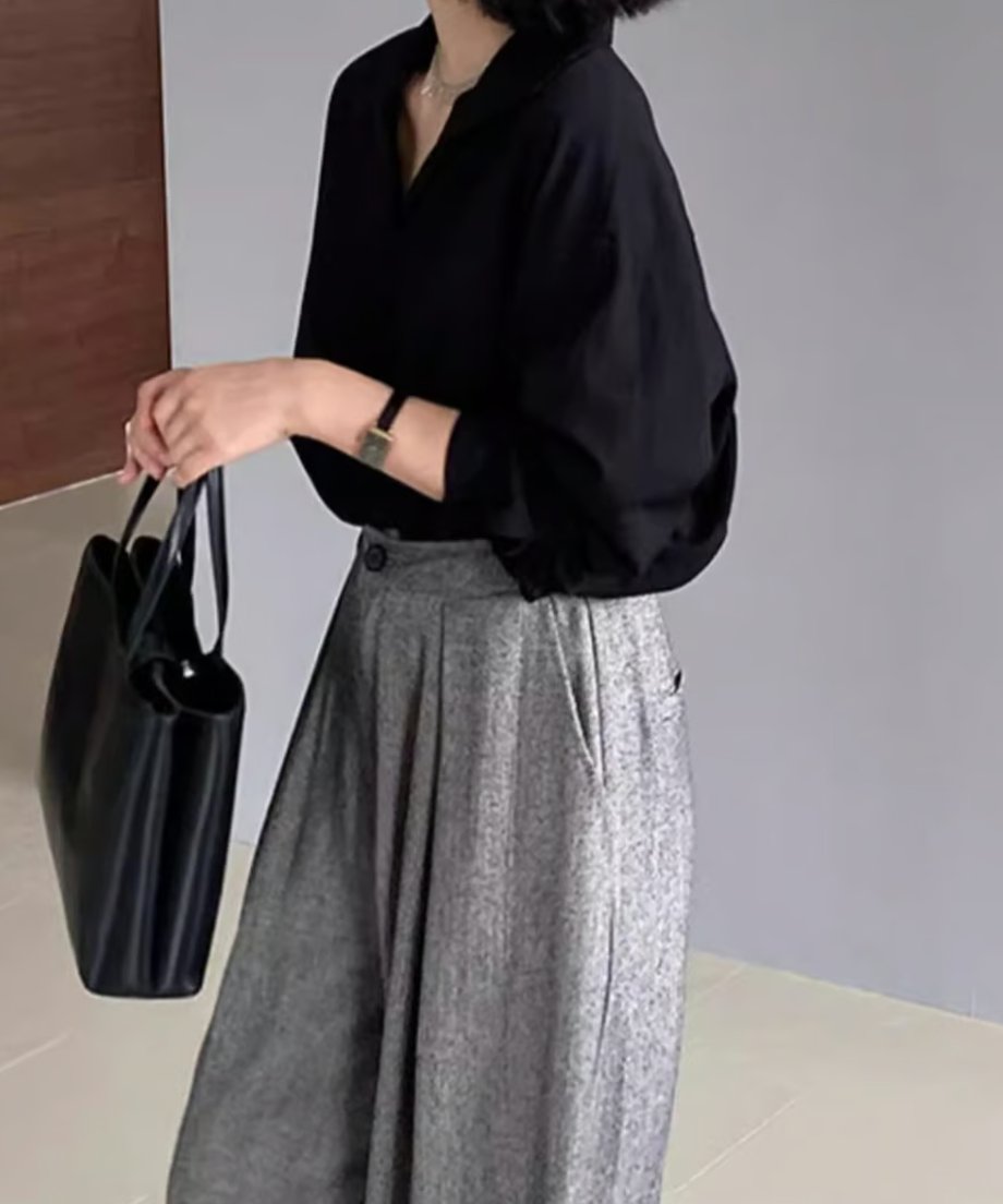 黒いシャツとライトグレーのワイドレッグパンツを着用し、黒いバッグを持った女性の全身の斜め前からのコーディネート。
