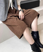 白シャツとグレーのベストに、茶色の太畝コーデュロイ膝丈ワイドパンツと黒のショートブーツを合わせた、白い階段に座る姿。