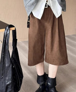 白シャツとグレーのベストに、茶色の太畝コーデュロイ膝丈ワイドパンツと黒のショートブーツを合わせた女性。隣のテーブルに黒いバッグがかかっている。