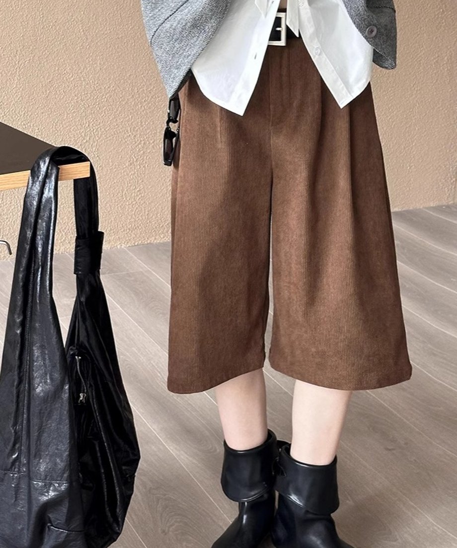 白シャツとグレーのベストに、茶色の太畝コーデュロイ膝丈ワイドパンツと黒のショートブーツを合わせた女性。隣のテーブルに黒いバッグがかかっている。