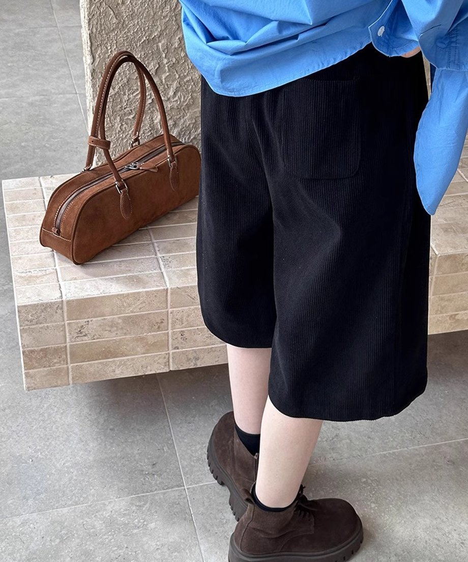 青いシャツを着用し、黒の太畝コーデュロイ膝丈ワイドパンツ（バックポケット付き）と茶色の厚底レースアップブーツを合わせたコーディネートの背面または斜め後ろからのクローズアップ。