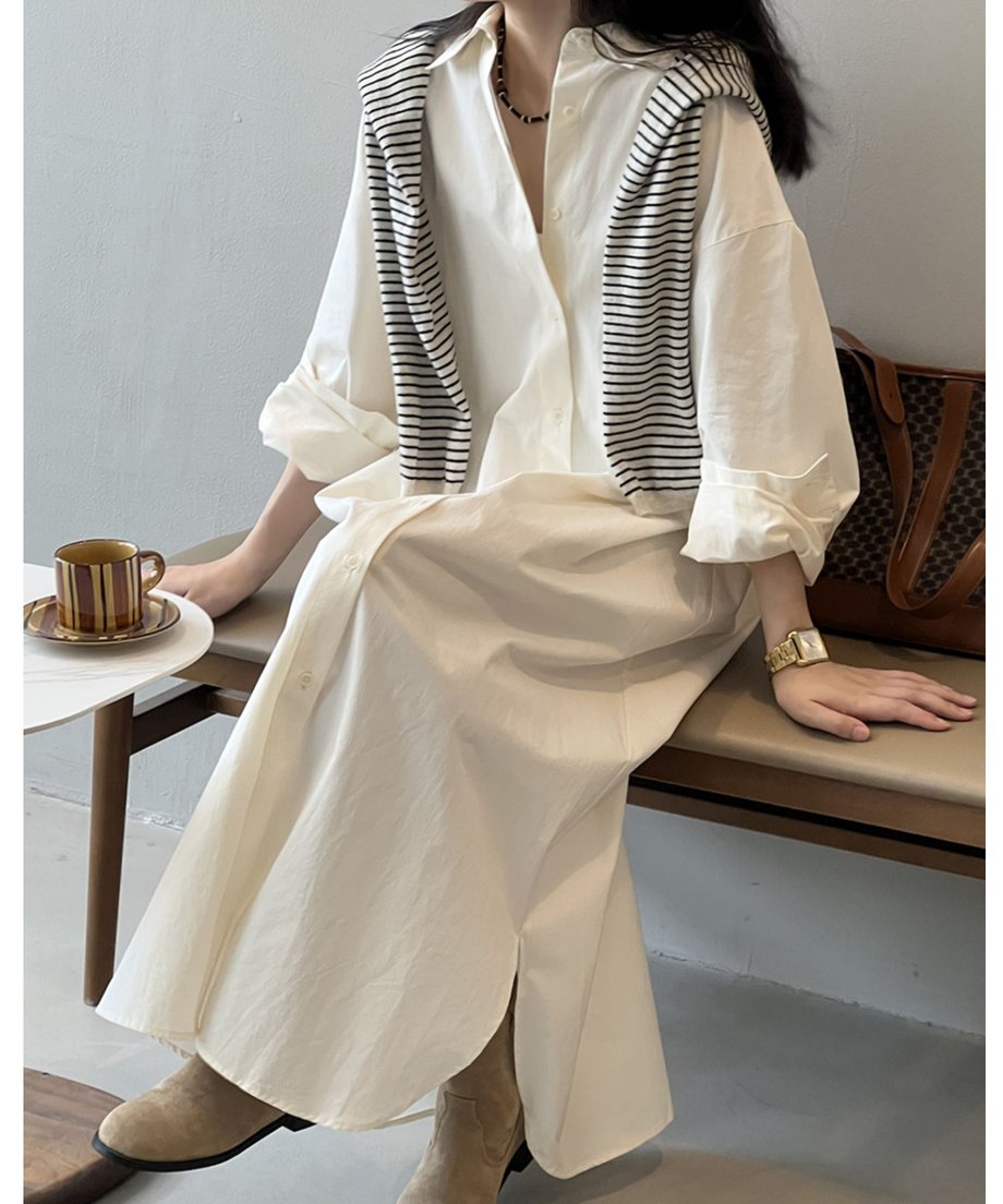 ベージュのロングシャツワンピースを着用した女性が椅子に座っている。足元はベージュのスエードブーツで、スリットが見える。