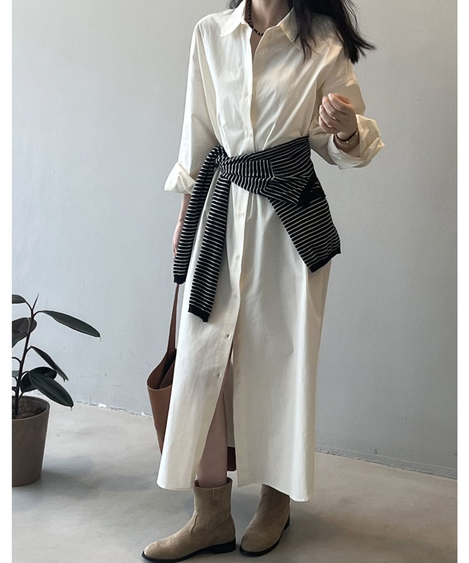 ベージュのロングシャツワンピースを着用した女性。ストライプ柄のニットをウエストで巻き、茶色のブーツを履いている。
