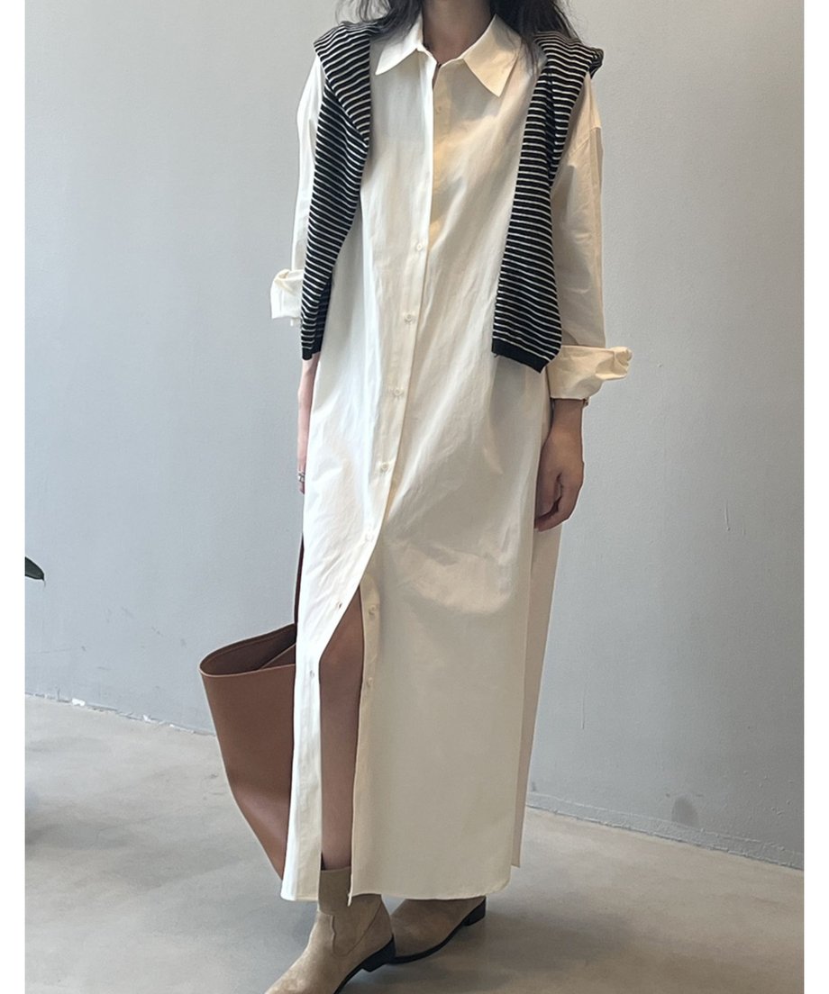 ベージュのロングシャツワンピースを着用した女性の全身。ボタンを開けてスリットを見せ、茶色のトートバッグとベージュのブーツを合わせている。