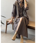 ダークグレーのロングシャツワンピースを着用した女性が椅子に座っている。インナーの白とストライプ柄のニットがアクセントになっている。