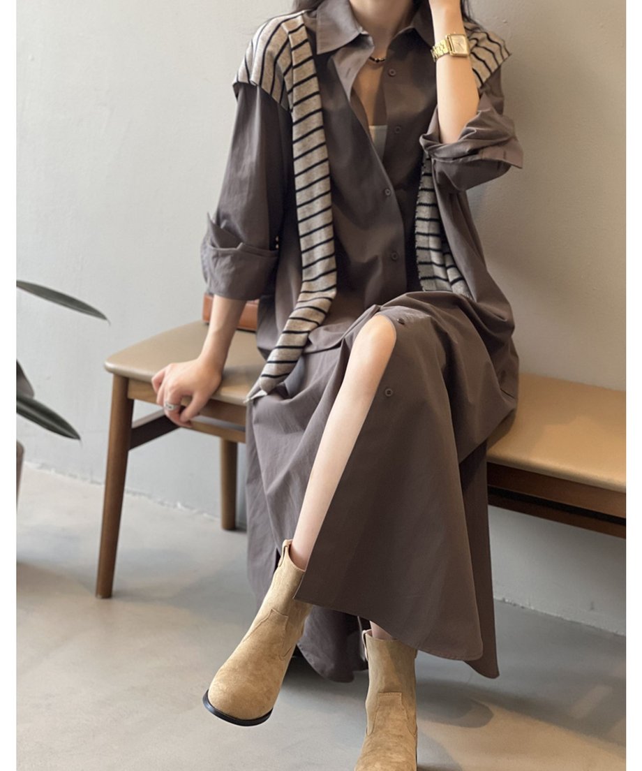ダークグレーのロングシャツワンピースを着用した女性が椅子に座っている。インナーの白とストライプ柄のニットがアクセントになっている。