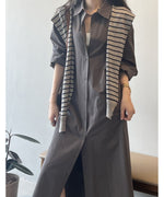 ダークグレーのロングシャツワンピースを着用した女性。インナーの白とストライプ柄のニットがアクセントになっている。