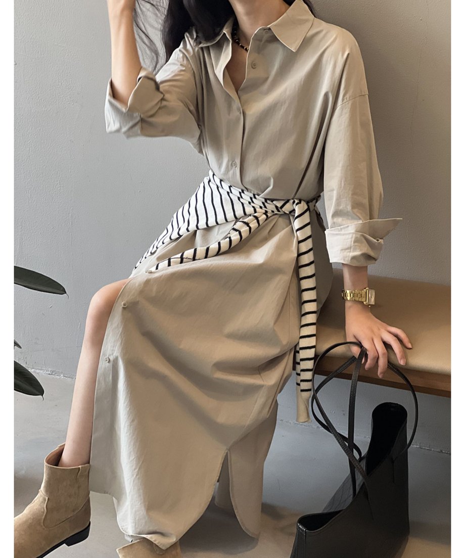 グレーのロングシャツワンピースを着用した女性が椅子に座っている。足元はベージュのスエードブーツで、スリットから膝下が見える。