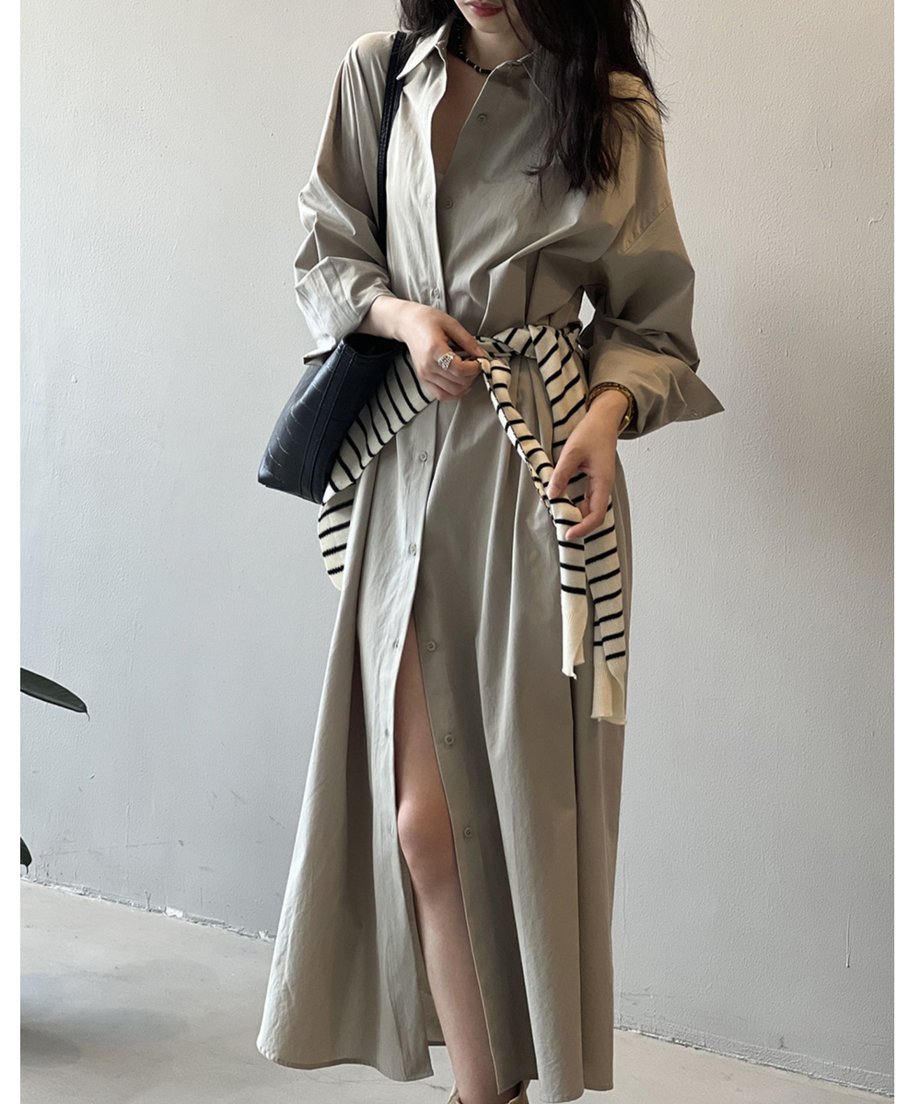 グレーのロングシャツワンピースを着用した女性が椅子に座っている。足元はベージュのスエードブーツで、スリットから膝下が見える。