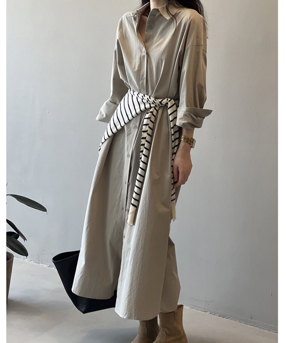 グレーのロングシャツワンピースを着用した女性が立っている正面画像。腰にボーダーのシャツを巻いている。