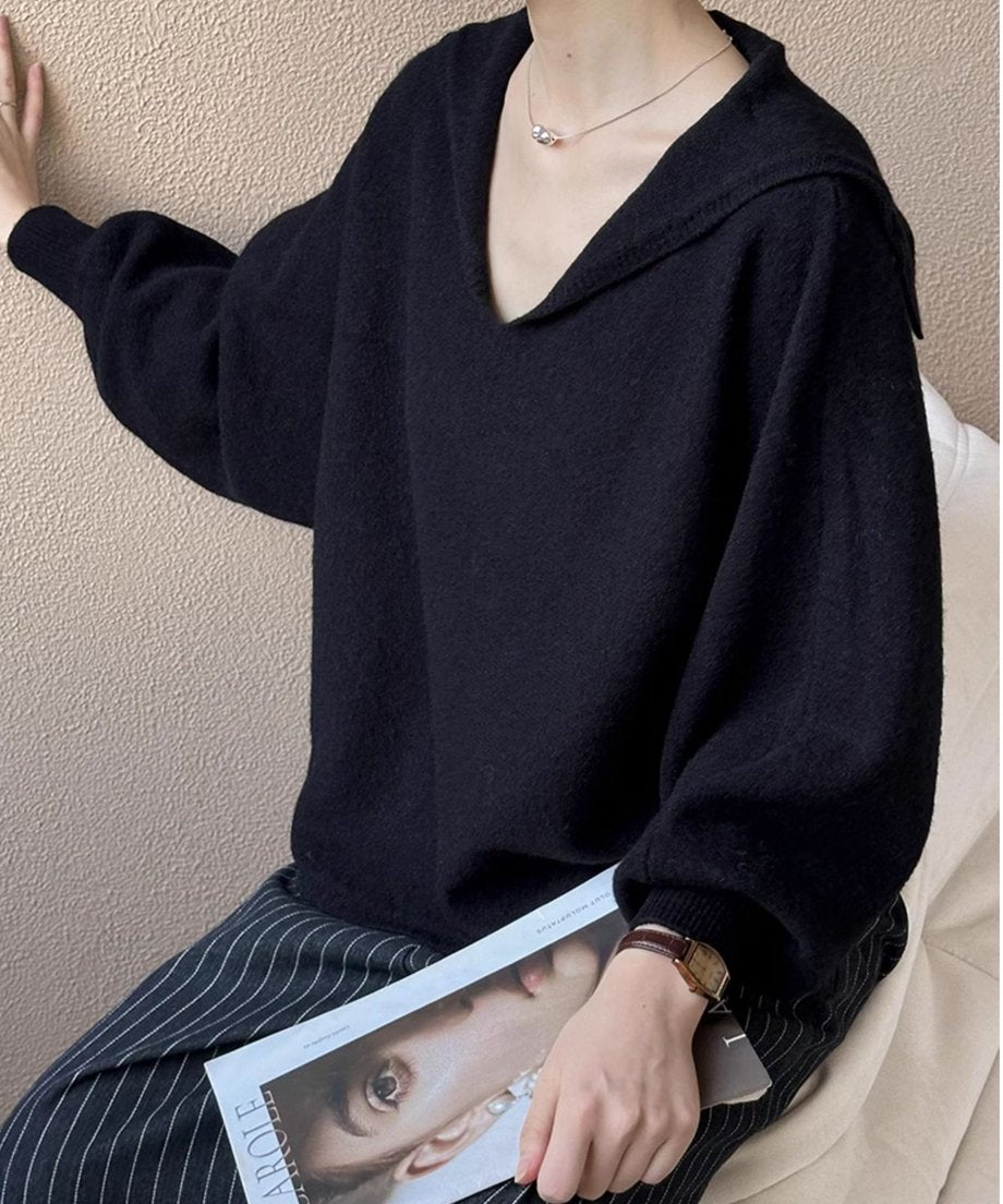 黒色のセーラーカラーVネックニットにストライプのパンツをコーディネートした女性が雑誌を持つ手のクローズアップ。