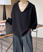 黒のセーラーカラーVネックニットにストライプ柄のワイドパンツを合わせ、雑誌を持った上半身のコーディネート。