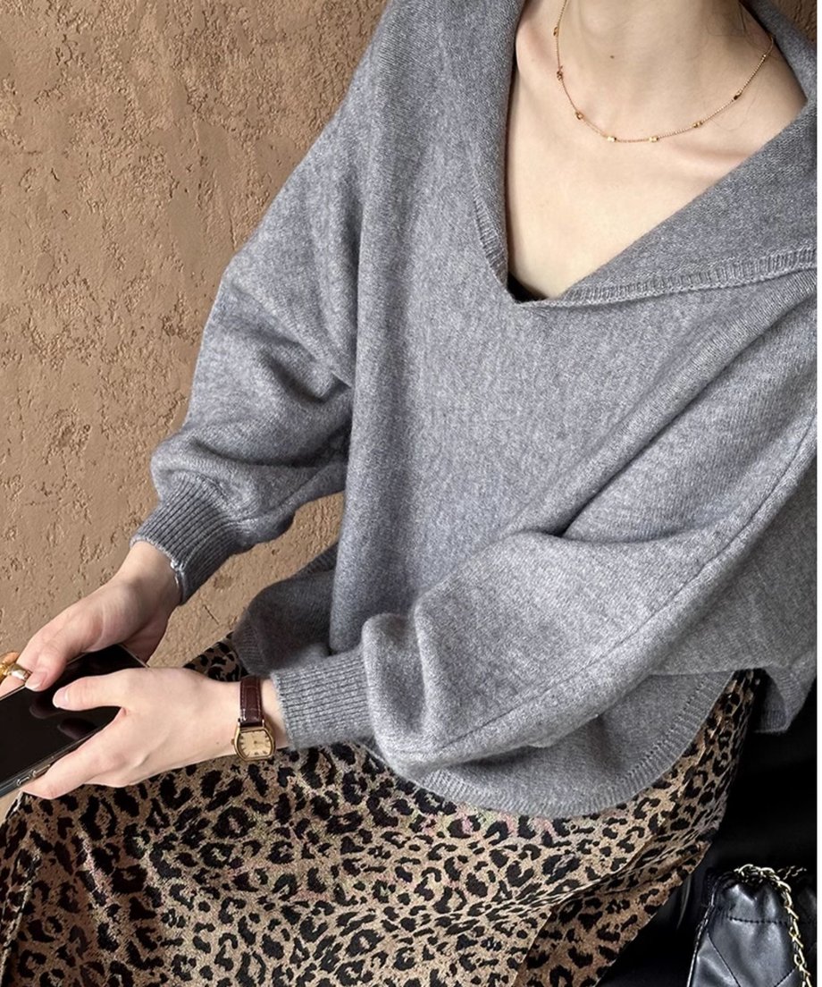 グレーのセーラーカラーVネックニットにレオパード柄のロングスカートを合わせた女性がスマホを手にもって座っている上半身のコーディネート。