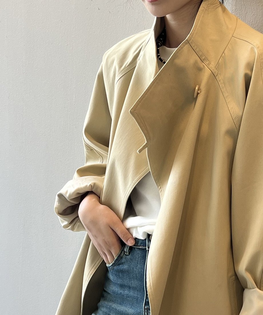 カーキ色のミドル丈コートのアップ。スタンドカラーとドロップショルダーのディテール、白Tシャツとデニムを合わせた着こなし。