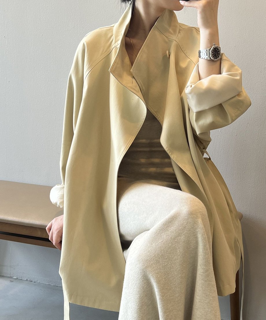 カーキ色のミドル丈コートを着用した女性の座り姿。時計をつけた腕とコートの襟周りのクローズアップ。