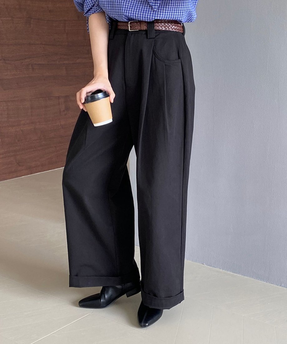 青と白のチェック柄のブラウスと茶色のベルトを着用したモデル。黒のワイドパンツを太めにロールアップし、片手にはカップを持っている。