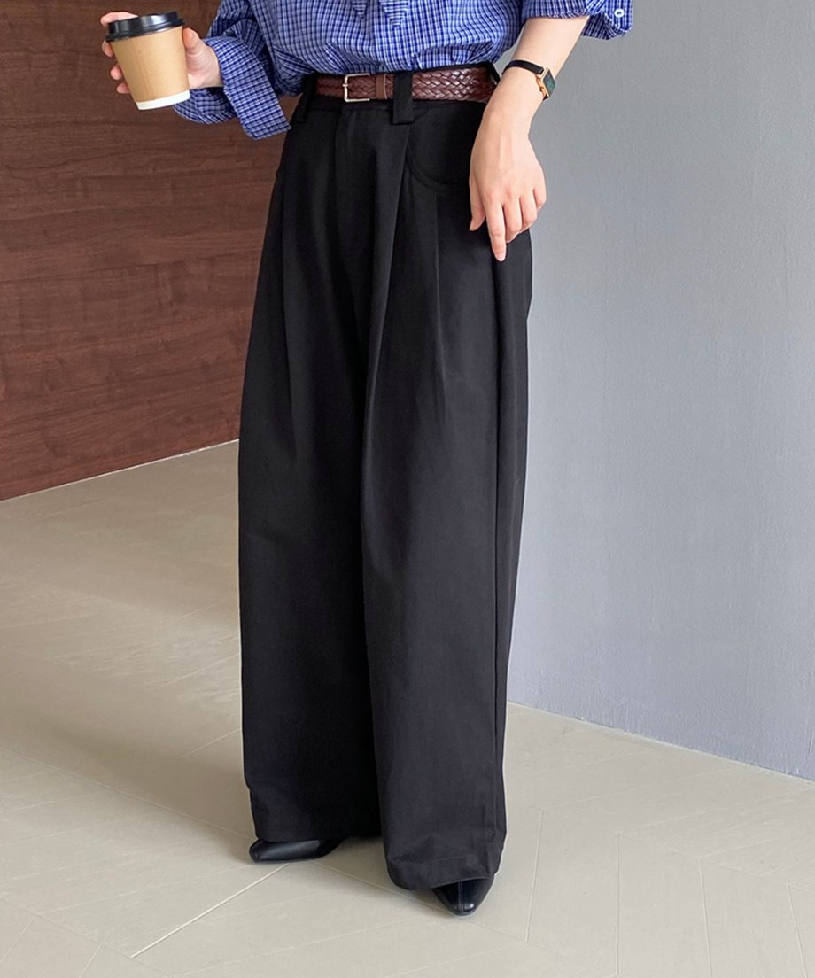 青いチェック柄のシャツに黒のワイドパンツをコーディネートした女性。ブラウンのベルトと手にカップを持った写真。