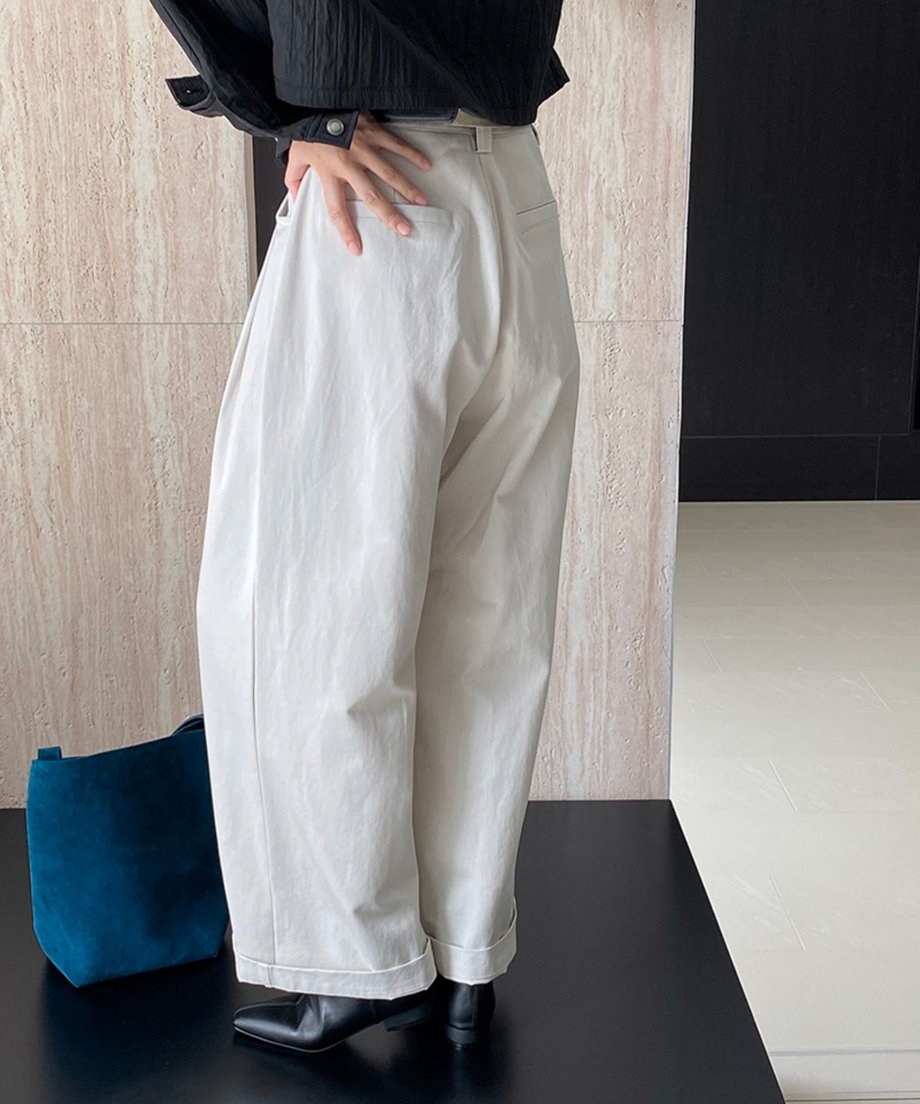 黒のジャケットと、フロントタックとロールアップが特徴のオフホワイトのストレートワイドパンツを着用したモデルの斜め後ろからのショット。